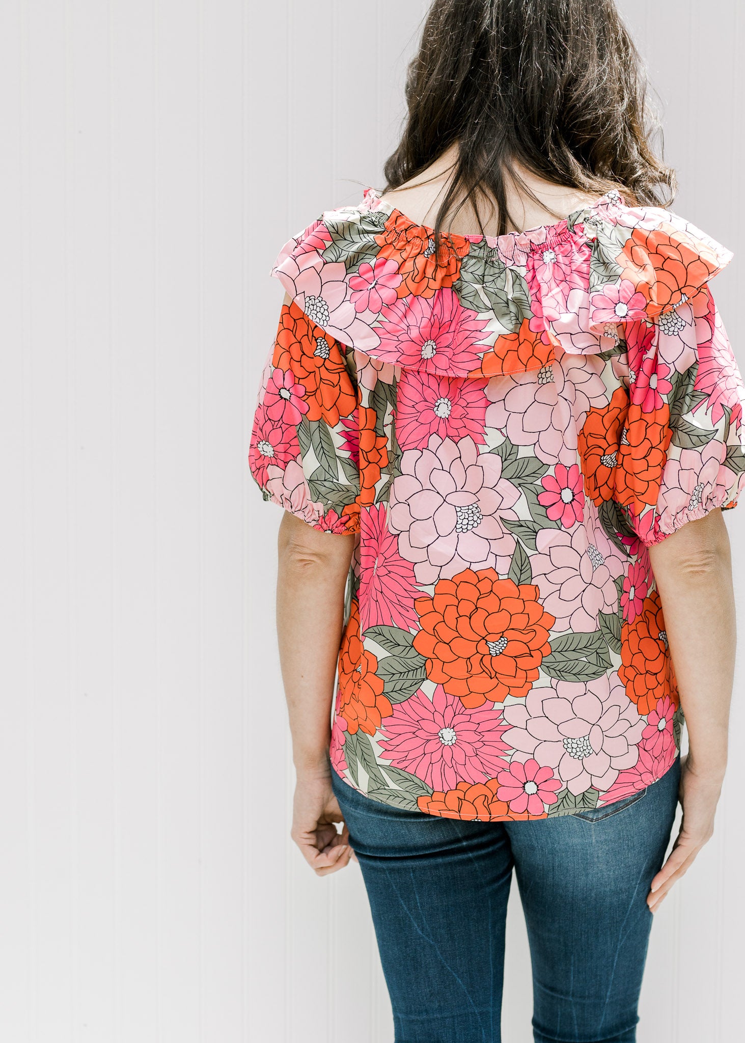 Back view of model wearing a fuchsia, red and pink floral top with bubble short sleeves. 
