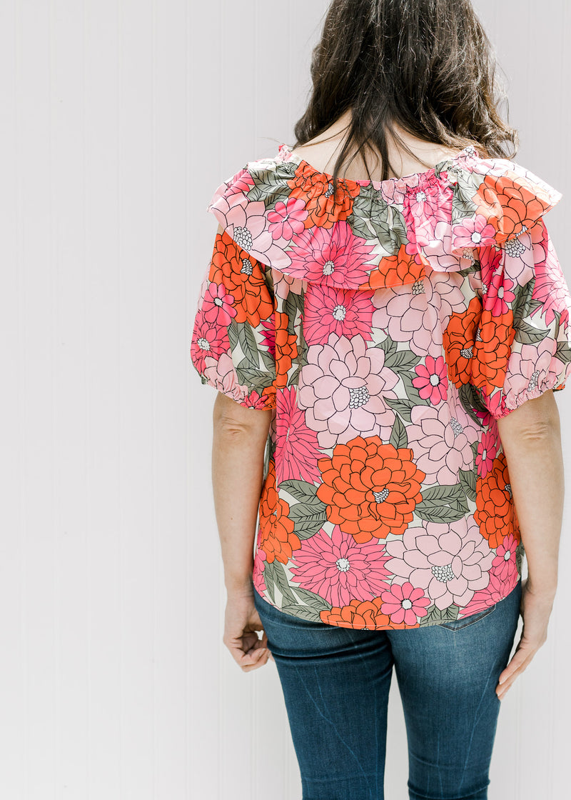 Back view of model wearing a fuchsia, red and pink floral top with bubble short sleeves. 