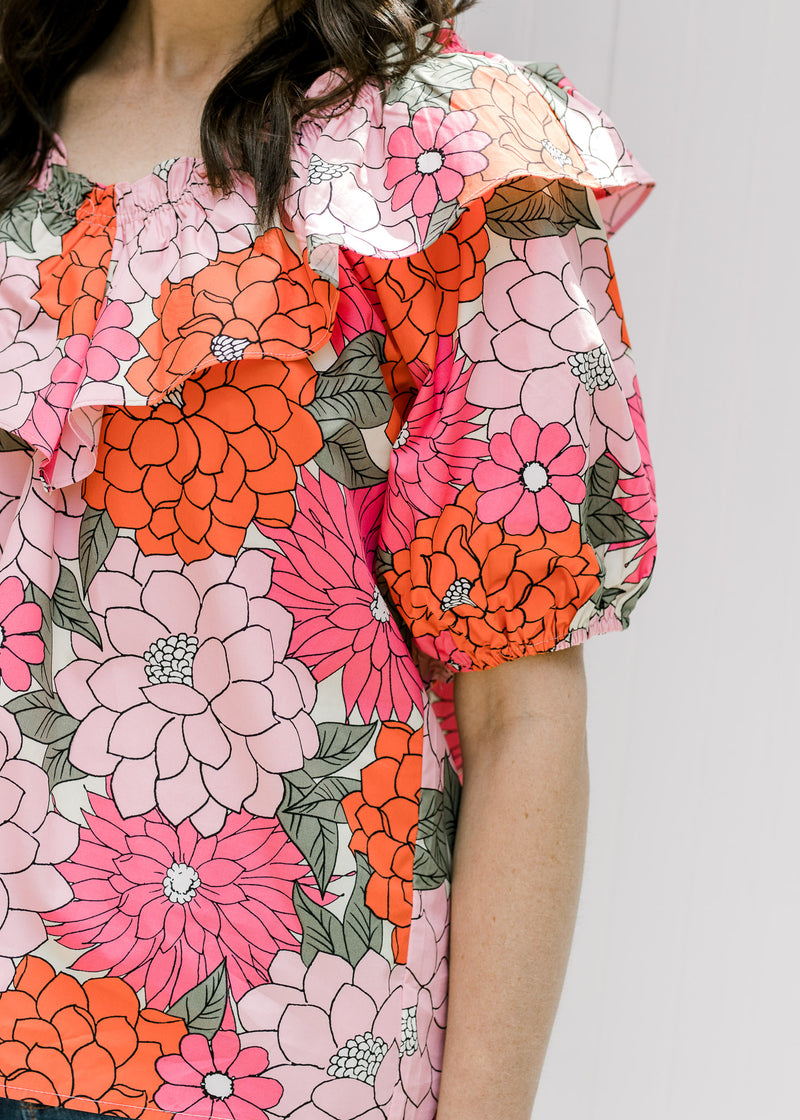 Close up view of bubble short sleeves and boat neck with a ruffle on a pink floral top. 