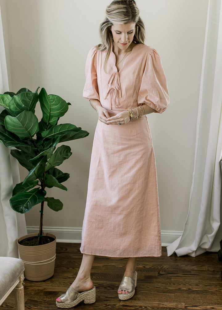 Model wearing a blush midi with short bubble sleeves, scalloped v-neck with tie and cinched waist. 