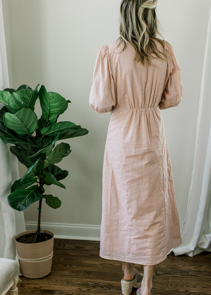 Back view of Model wearing a blush midi with short bubble sleeves and cinched waist. 