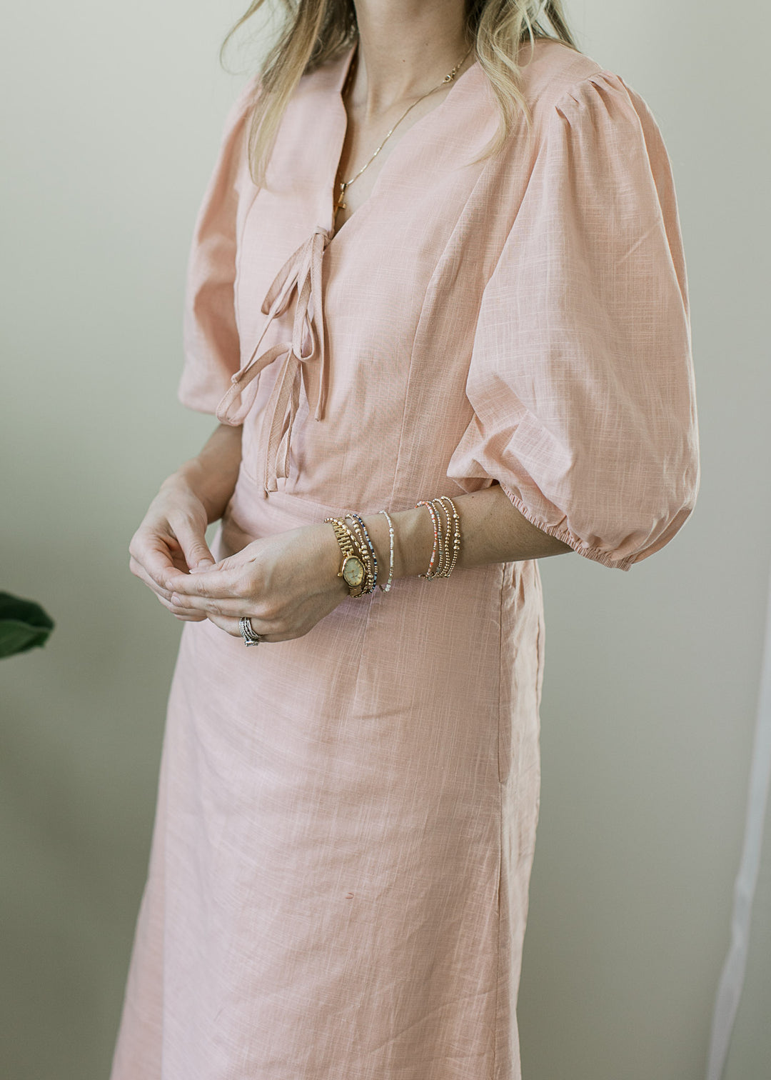 Close up of scalloped v-neck with ties and pleated shoulders on bubble sleeves of a blush midi. 