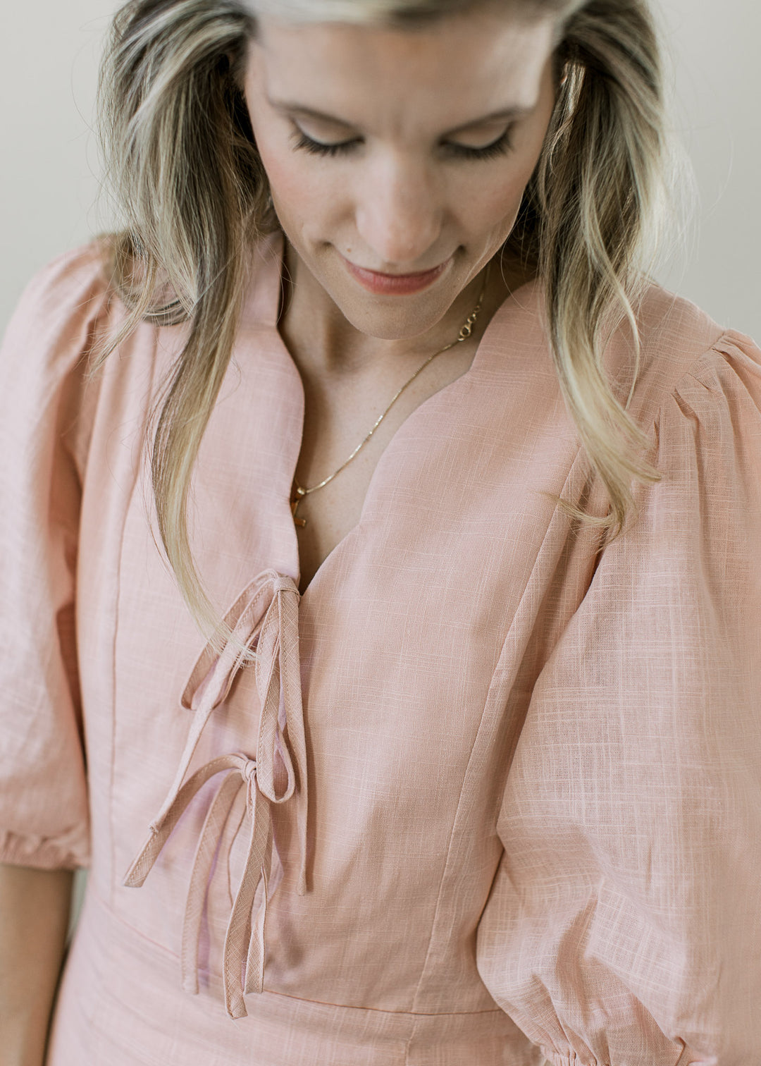 Close up of scalloped v-neck with two ties on a blush fully lined midi with short sleeves. 