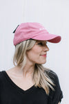 Side view of Model wearing an blue adjustable size hat with embroidered script mama with a pink bow.