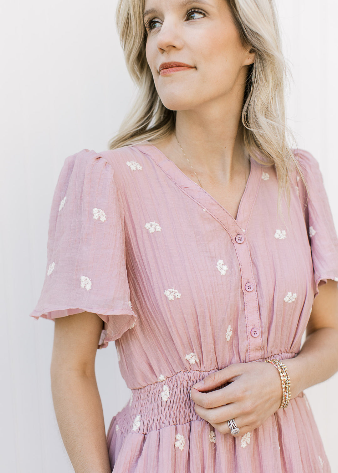 Close up of v-neck, buttons and smocked waist on a pink midi with embroidered white flowers. 