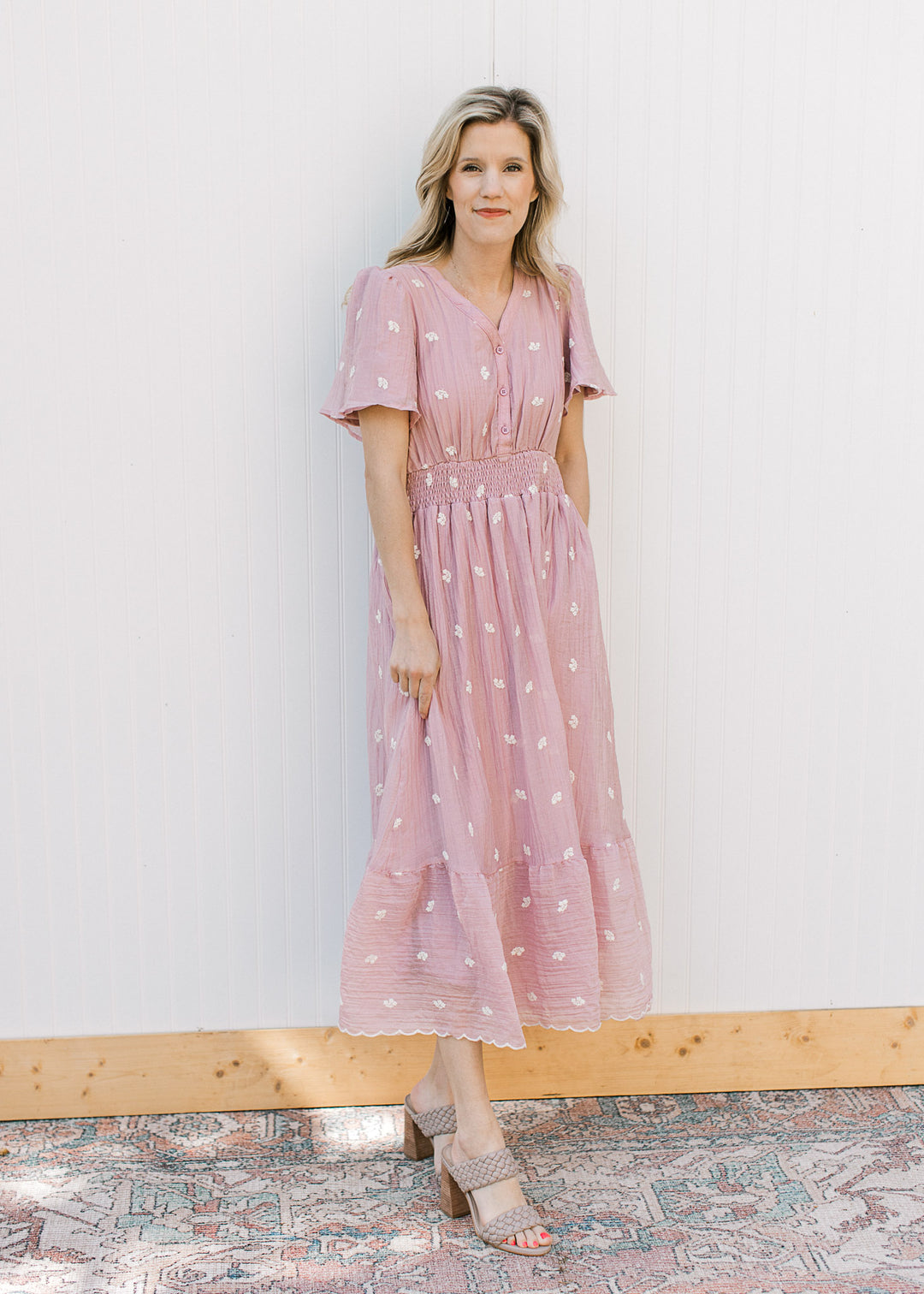 Model wearing a pink short sleeve midi with embroidered white flowers and a smocked waist.