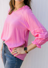 Model wearing a bright pink top with a v-neck, 3/4 sleeve and ruffle details at neck and sleeve.