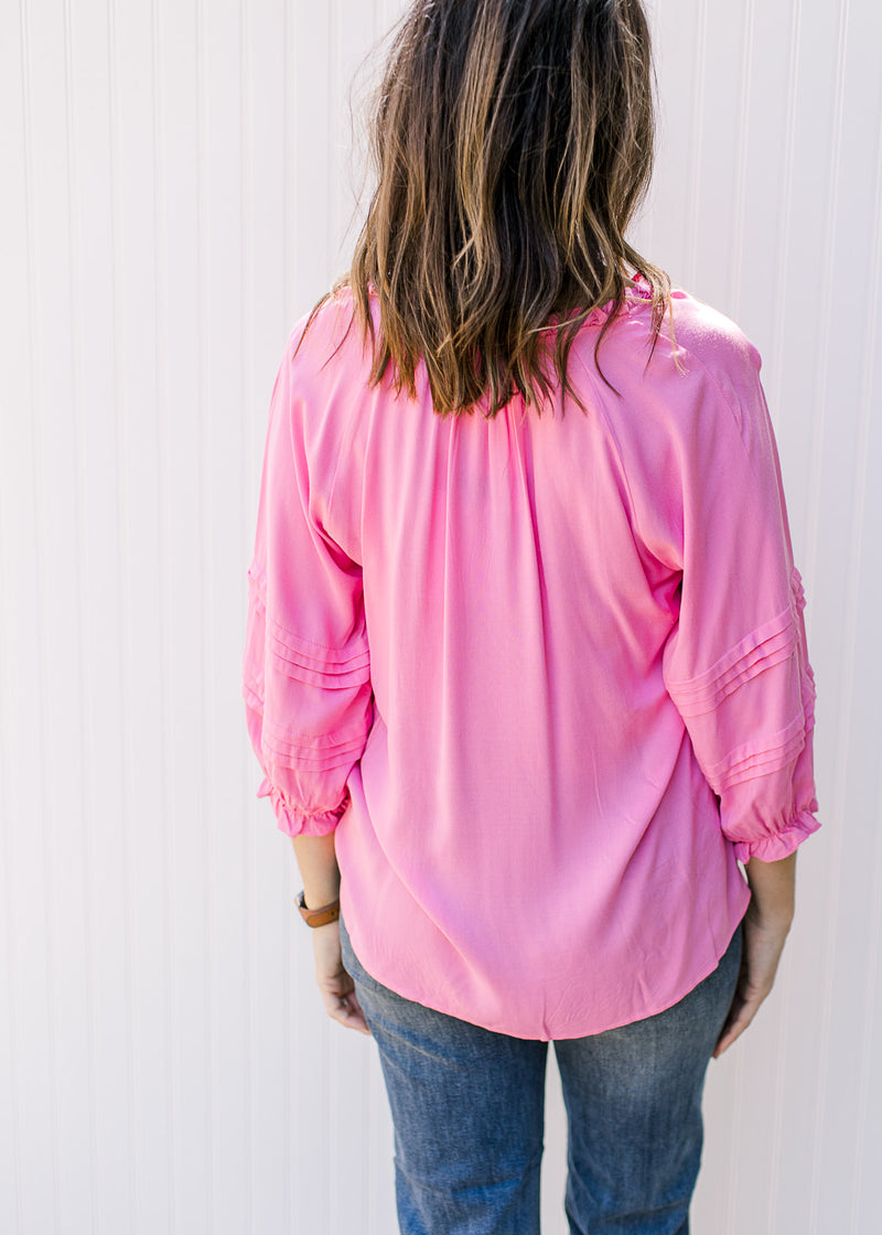 Back view of a bright pink top with 3/4 sleeves and ruffle at neck and sleeve. 