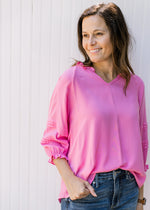 Model wearing jeans and a bright pink top  with 3/4 sleeves, v-neck and ruffle at sleeve and neck.