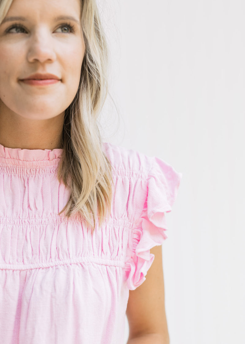 Close up view of cap sleeve with ruffle and smocked detail at bust on a pink top. 