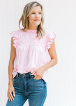Model wearing a pink top with a smocked detail at bust and a capped sleeve with a ruffle. 