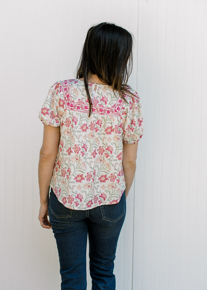 Back view of Model wearing a cream top with pink, yellow and green floral and bubble short sleeves.