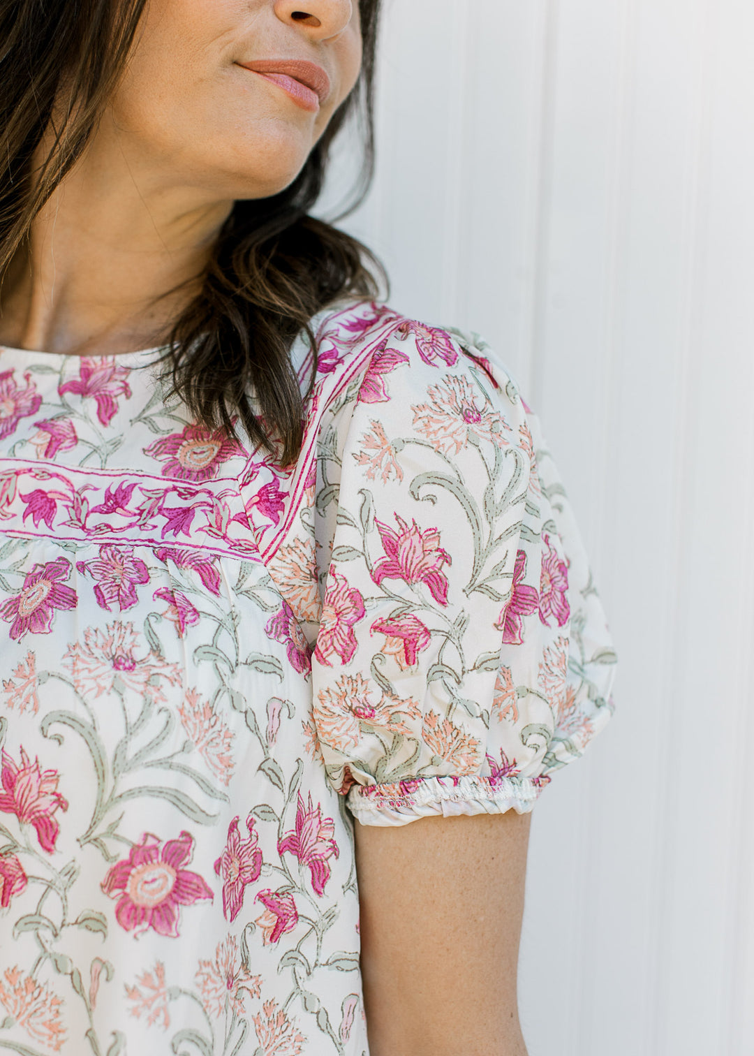 Close up of bubble short sleeves on a cream top with pink, yellow and green floral and a round neck.