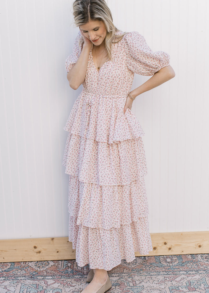 Model wearing a pale pink maxi with ditsy floral, tie at the waist, ruffle tiers and short sleeve.