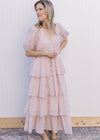 Model wearing flats and a pale pink maxi with floral, tie waist, ruffle tiers and short sleeve.