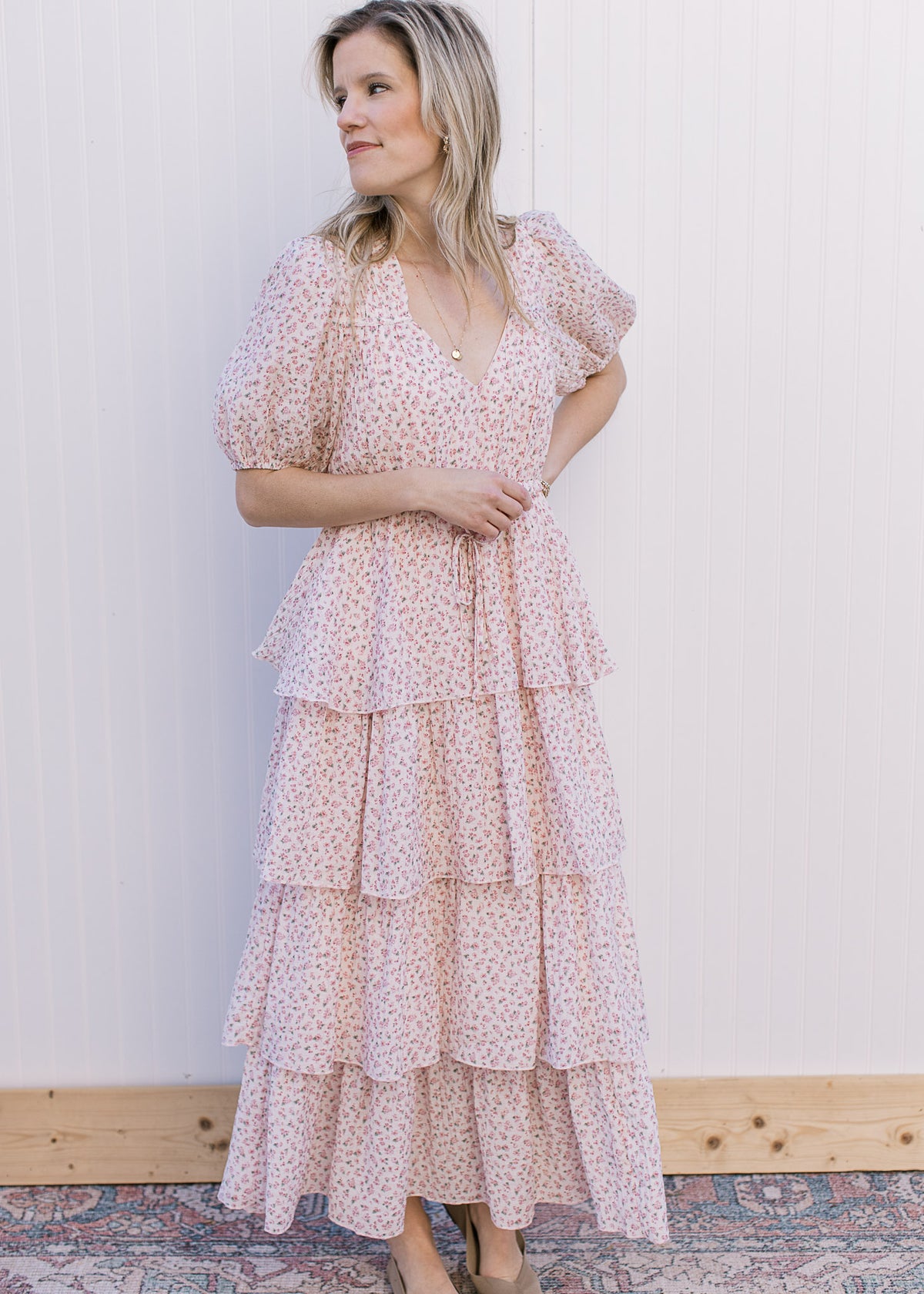 Model wearing flats and a pale pink maxi with floral, tie waist, ruffle tiers and short sleeve.
