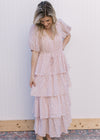 Model wearing a pale pink v-neck maxi with ditsy floral, tie waist and ruffled tiers.