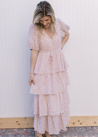Model wearing a pale pink v-neck maxi with ditsy floral, tie waist and ruffled tiers.