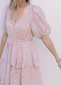 Close up of v-neck, bubble short sleeves and tie waist on a pale pink maxi with ditsy floral. 