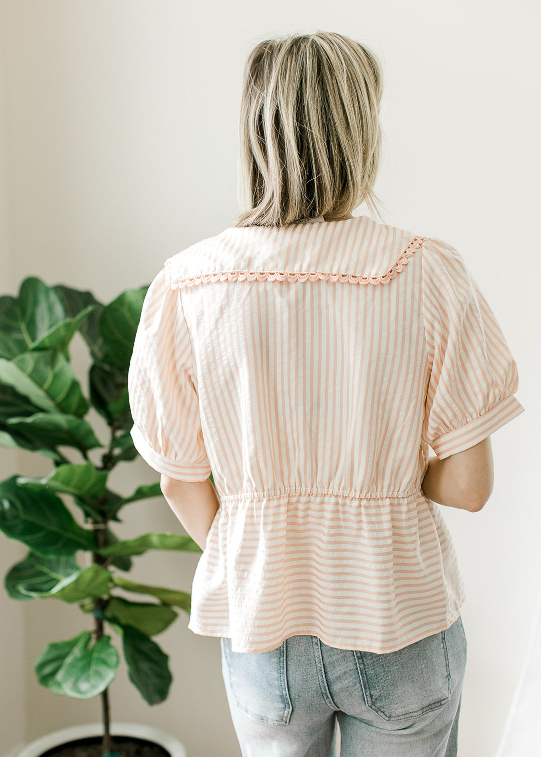 Back view of Model wearing a pink and cream striped peplum top with short sleeves and collar.