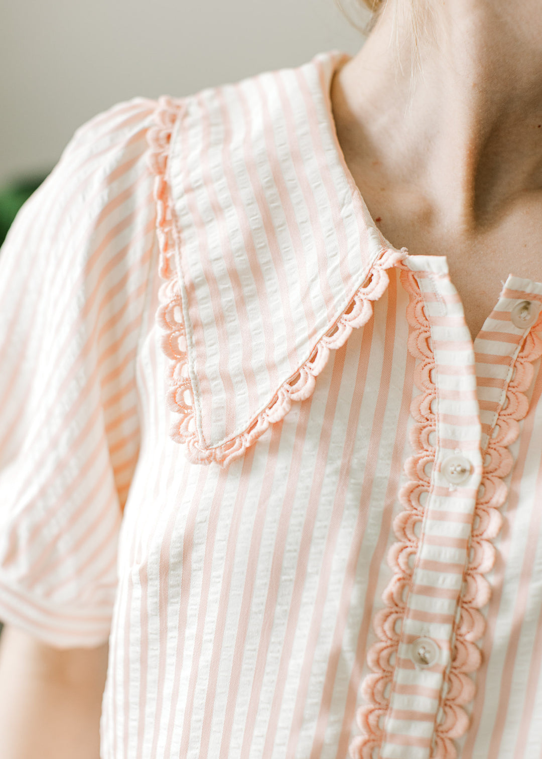 Close up of collar and button placket with scalloped edges on a pink and cream striped top.