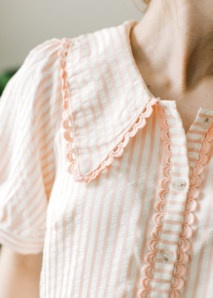 Close up of collar and button placket with scalloped edges on a pink and cream striped top.