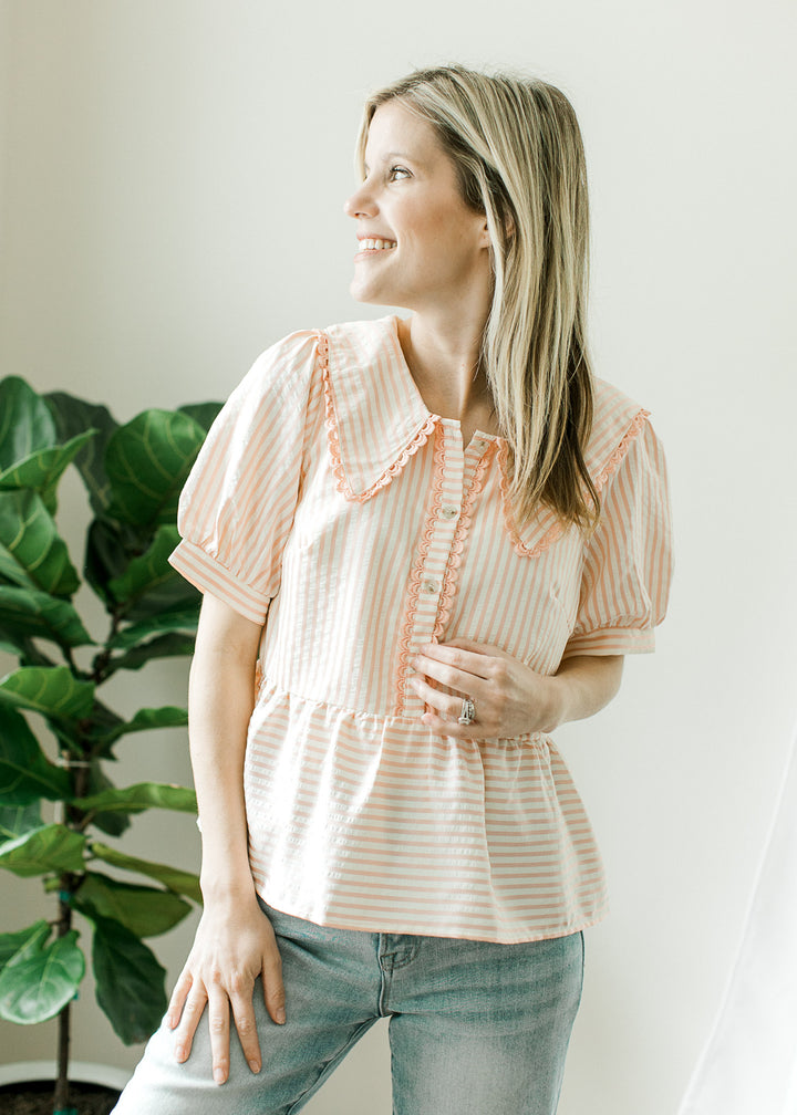 Model wearing a pink and cream striped short sleeve top with elastic waist and a collar.