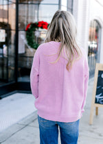 Back view of Model wearing a pink sweater with long sleeves and two styles of textured knit 