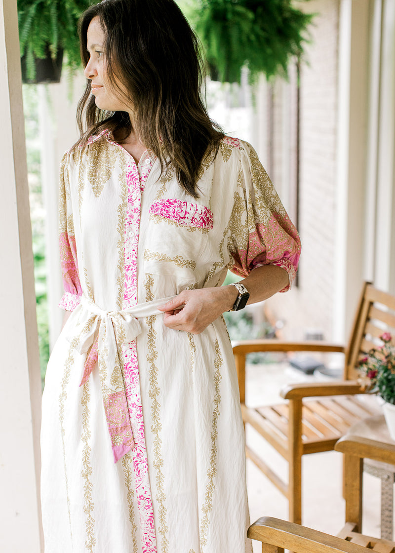 Model wearing a cream midi with gold and pink print, bubble short sleeves, buttons and a tie waist. 