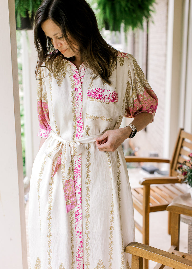 Model wearing a cream midi with gold and pink print, short sleeves, patch pocket and tie waist. 