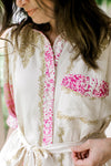 Close up of patch pocket, buttons and tie at the waist of a cream midi with gold and pink print. 