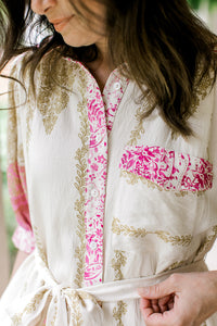 Close up of patch pocket, buttons and tie at the waist of a cream midi with gold and pink print. 