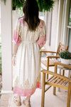 Back view of Model wearing a cream midi with gold and pink print, bubble short sleeves and buttons. 