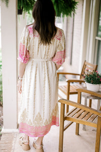 Back view of Model wearing a cream midi with gold and pink print, bubble short sleeves and buttons. 