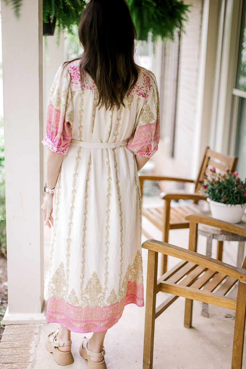 Back view of Model wearing a cream midi with gold and pink print, bubble short sleeves and buttons. 