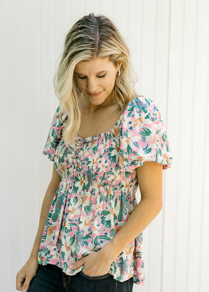 Model wearing a pink floral babydoll top with puff short sleeves and a smocked bodice. 