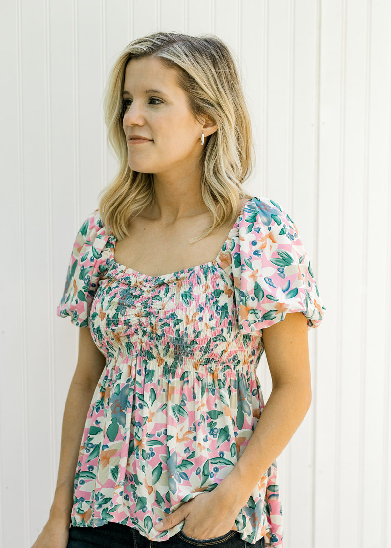Model wearing jeans with a pink floral babydoll top with puff short sleeves and a smocked bodice. 