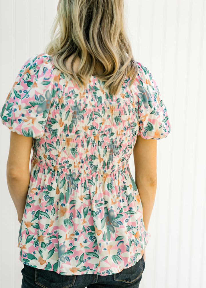 Back view of Model wearing a pink floral babydoll top with puff short sleeves and a smocked bodice. 