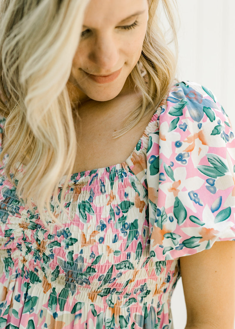 Close up view of a model wearing a pink floral top with puff short sleeves and a smocked bodice. 