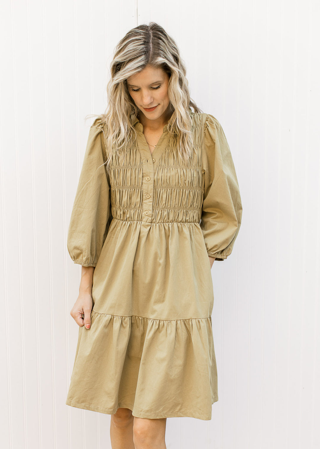 Model wearing a greenish-brown above the knee dress with a smocked bodice and 3/4 bubble sleeves.
