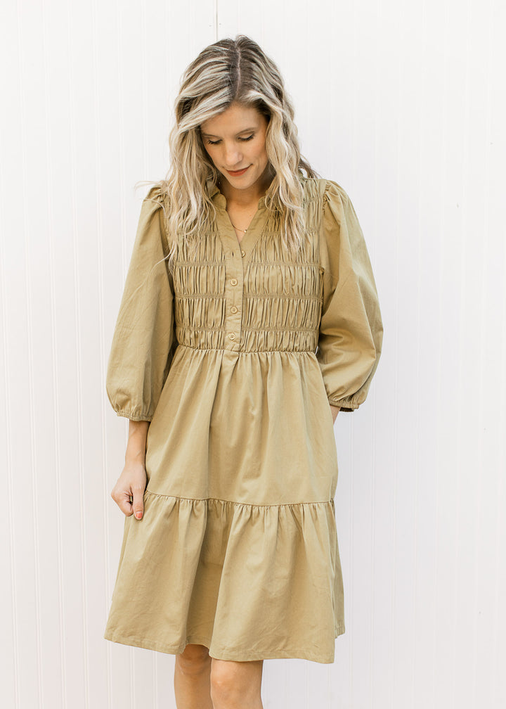 Model wearing a greenish-brown above the knee dress with a smocked bodice and 3/4 bubble sleeves.