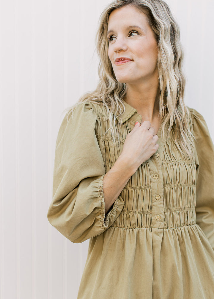 Close up on smocked bodice with buttons, v-neck and a collar on a greenish-brown dress. 