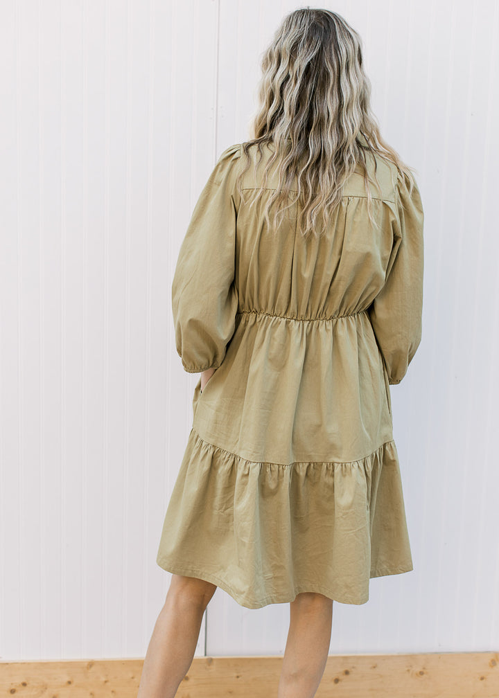 Back view of Model wearing a greenish-brown dress with an elastic waist and 3/4 bubble sleeves.