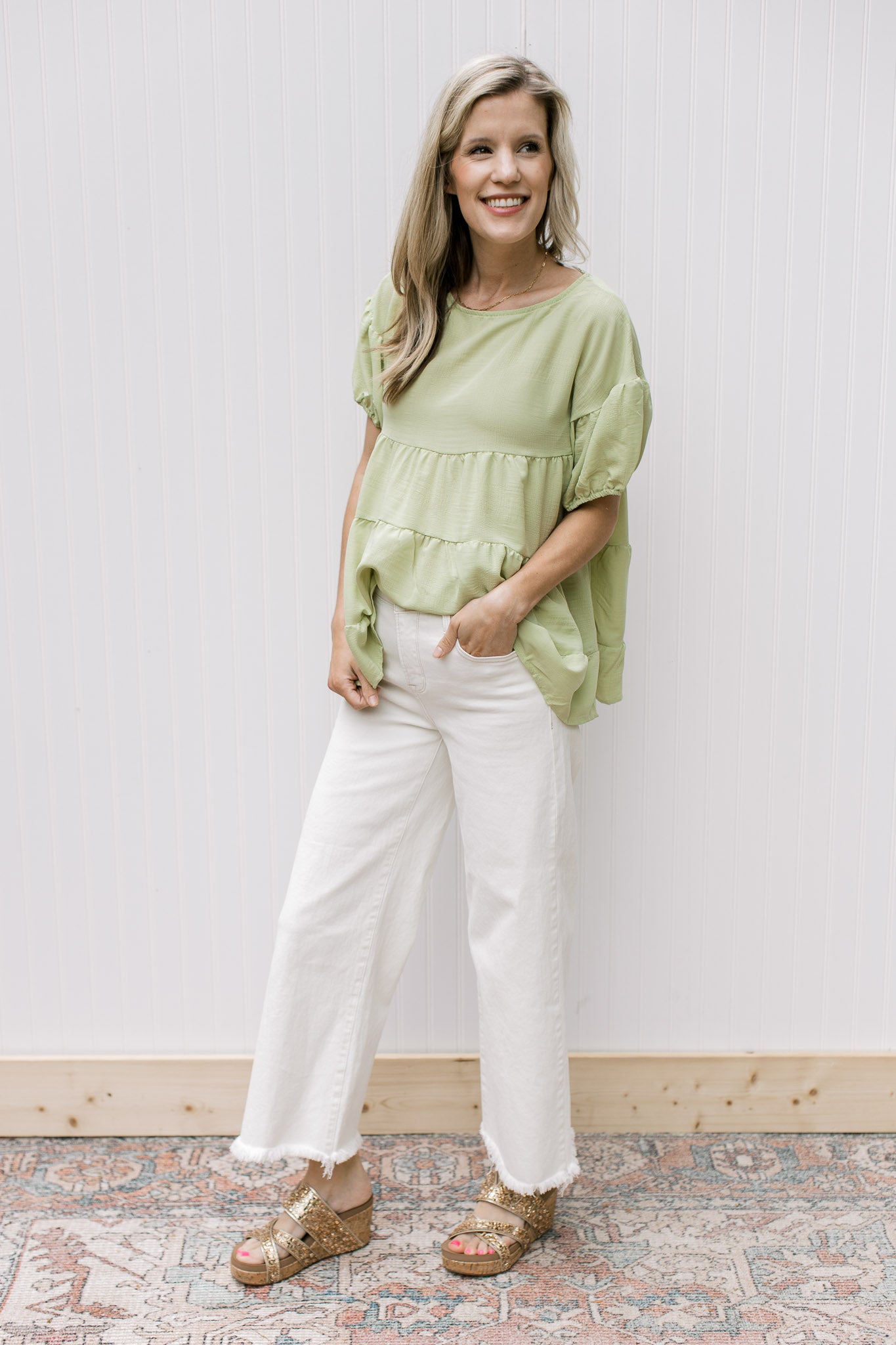 Model wearing white jeans, wedges and  a tiered top with balloon short sleeve and a keyhole.