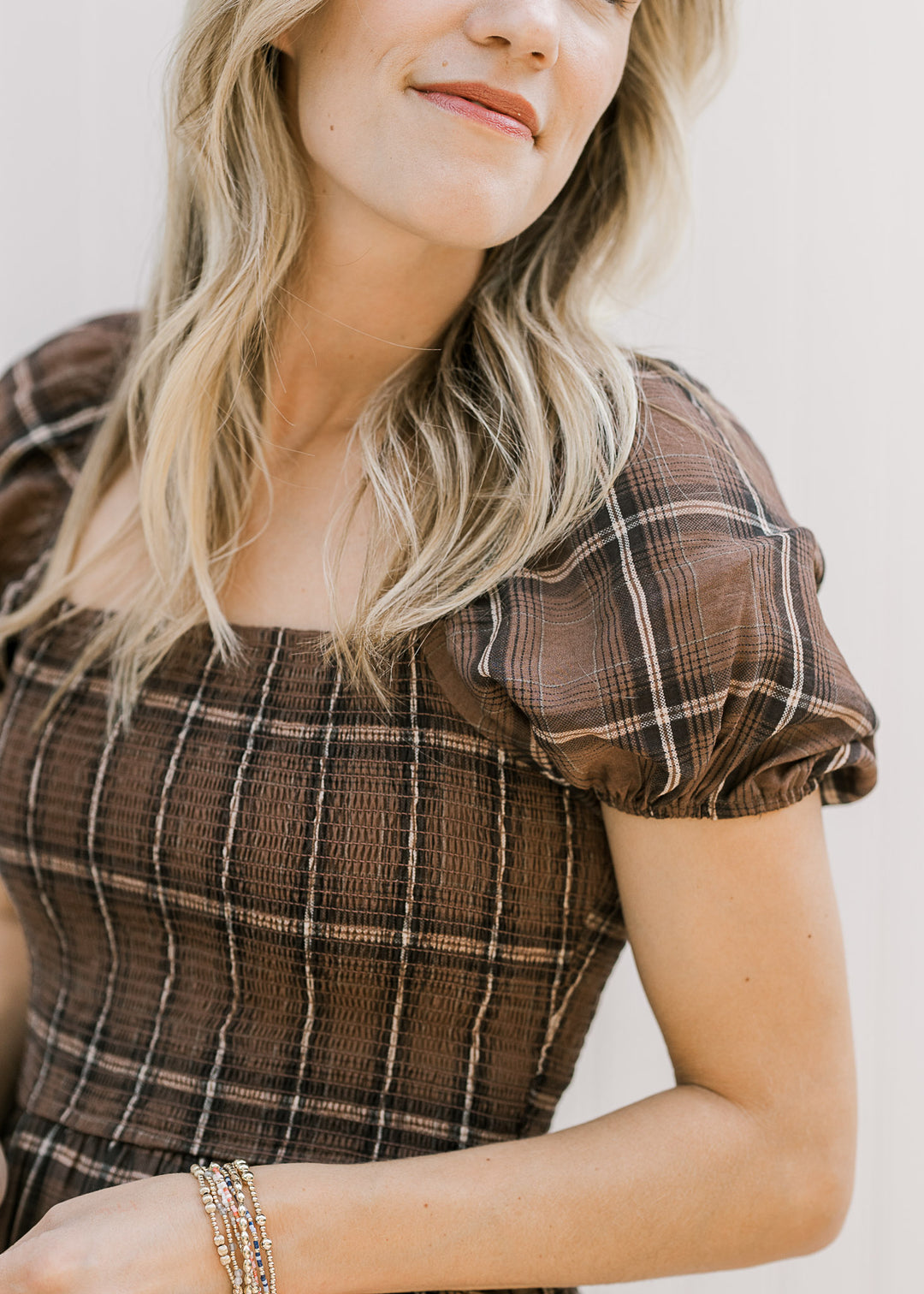 Close up of smocked bodice and short puff sleeves on a model in a brown and cream plaid midi.