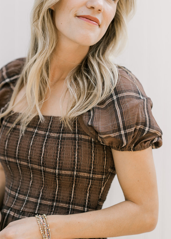 Close up of smocked bodice and short puff sleeves on a model in a brown and cream plaid midi.