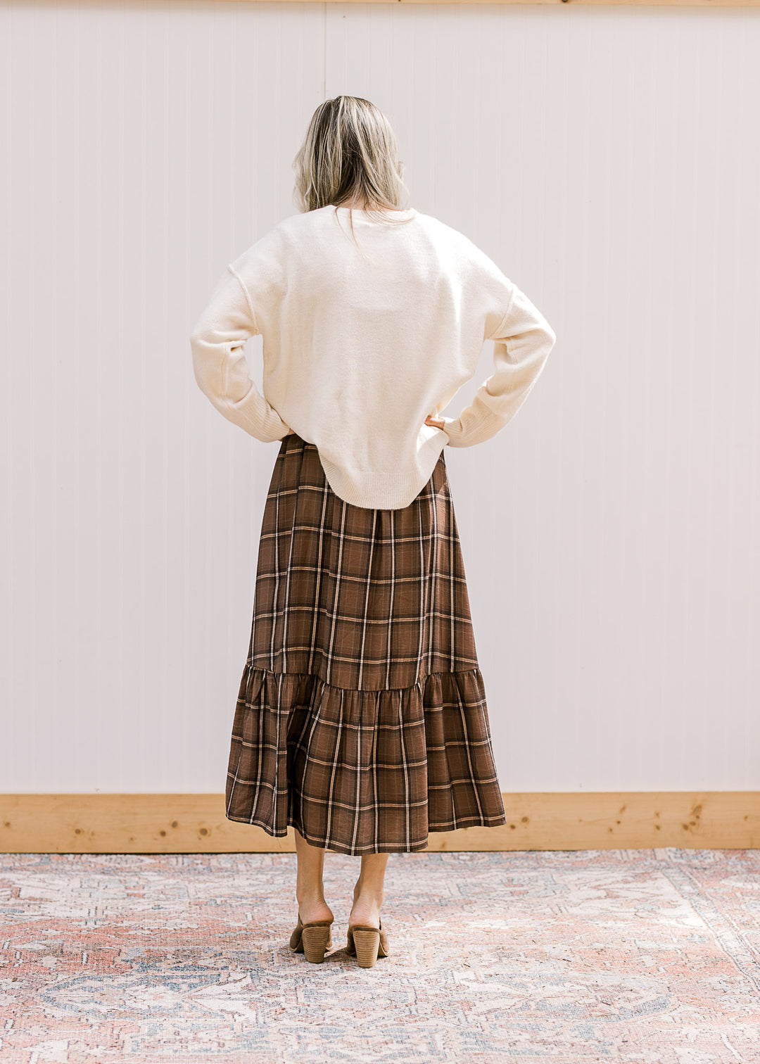 Back view of model wearing a cream sweater over a brown and cream plaid midi. 