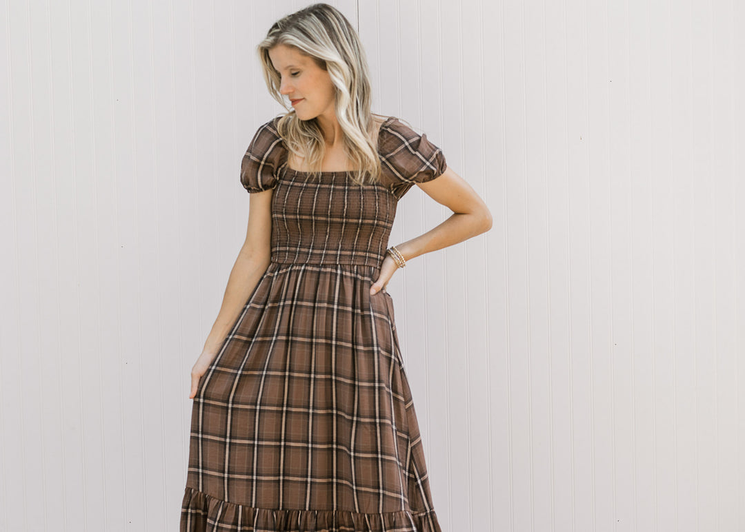 Model wearing a brown and cream plaid midi with a smocked bodice, square neck and short sleeves. 