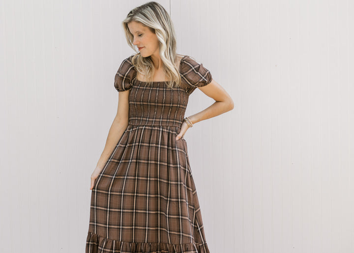 Model wearing a brown and cream plaid midi with a smocked bodice, square neck and short sleeves. 