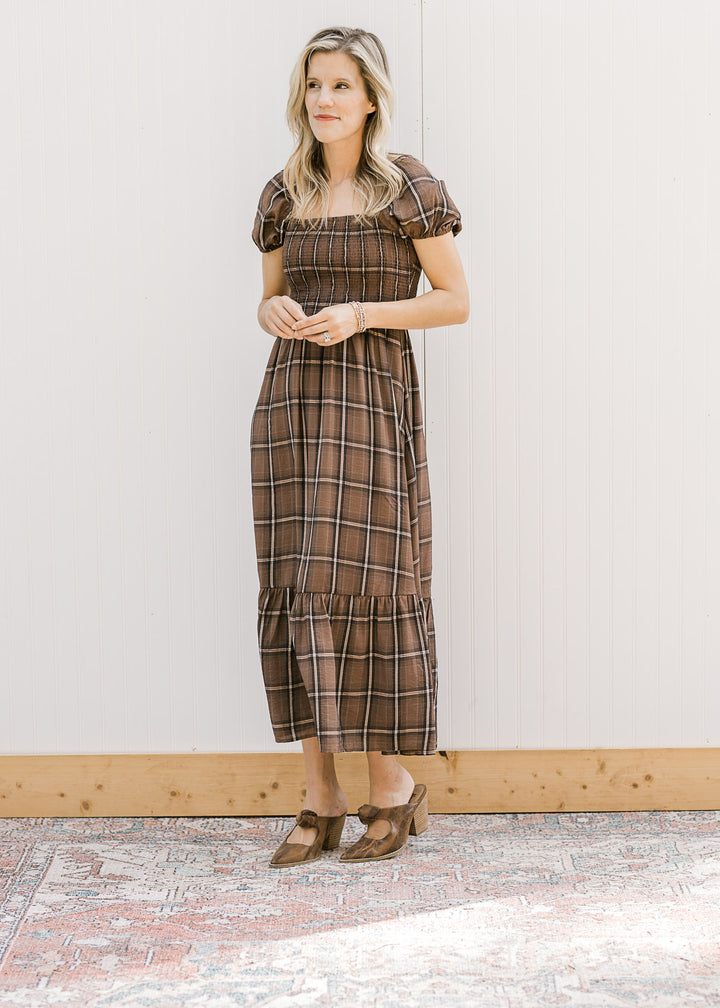 Model wearing a brown and cream plaid midi with a smocked bodice and short puff sleeves. 